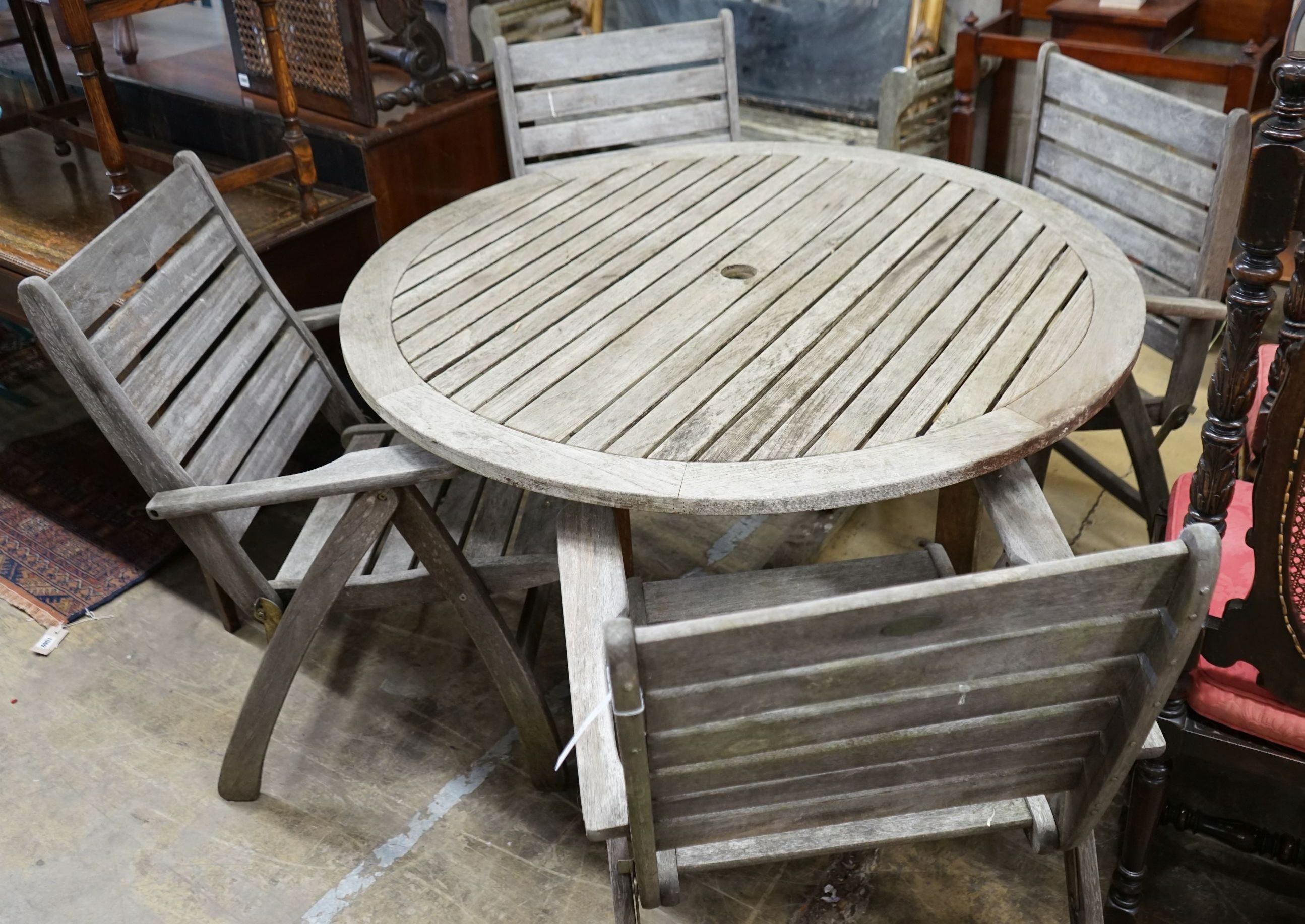 A circular weathered teak slatted garden table, diameter 122cm, height 74cm together with four weathered teak folding garden armchairs
